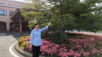 正面玄関前にある40周年記念植樹の木を指す萩原なつ子の写真